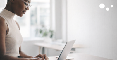 Black woman working on a laptop. Wageindicator logo of three orbs at top-right corner.